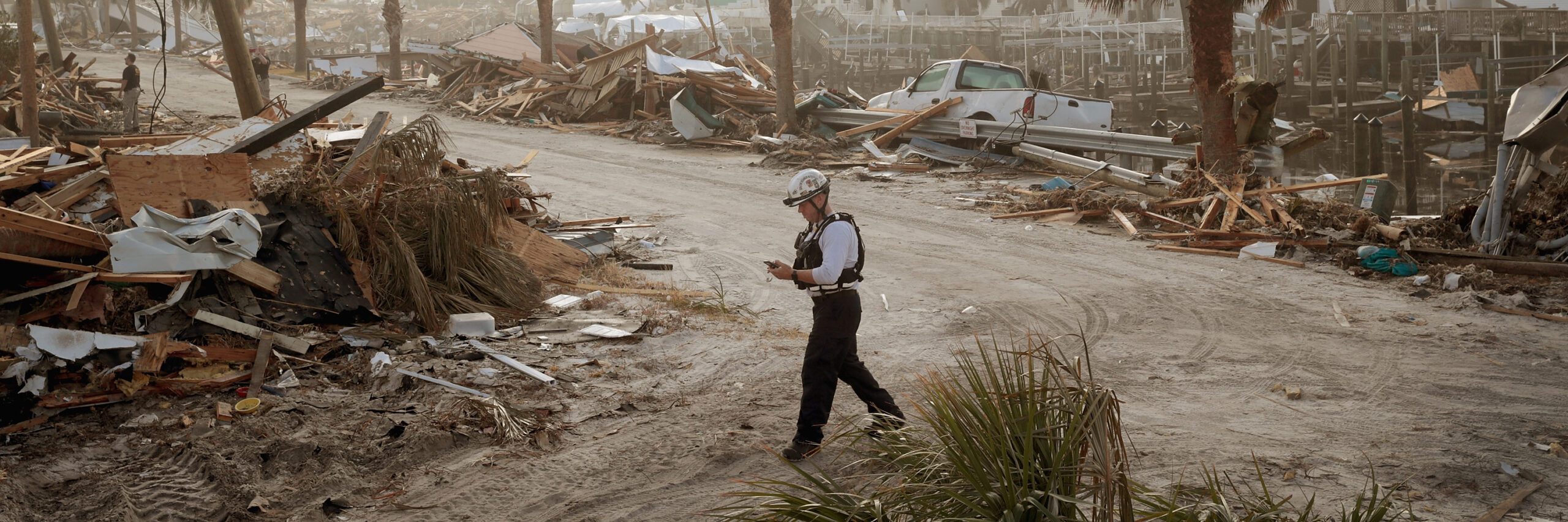 A man walks along a road littered with debris, reflecting the aftermath of Hurricane Michael, ongoing disaster recovery, and emergency management efforts.