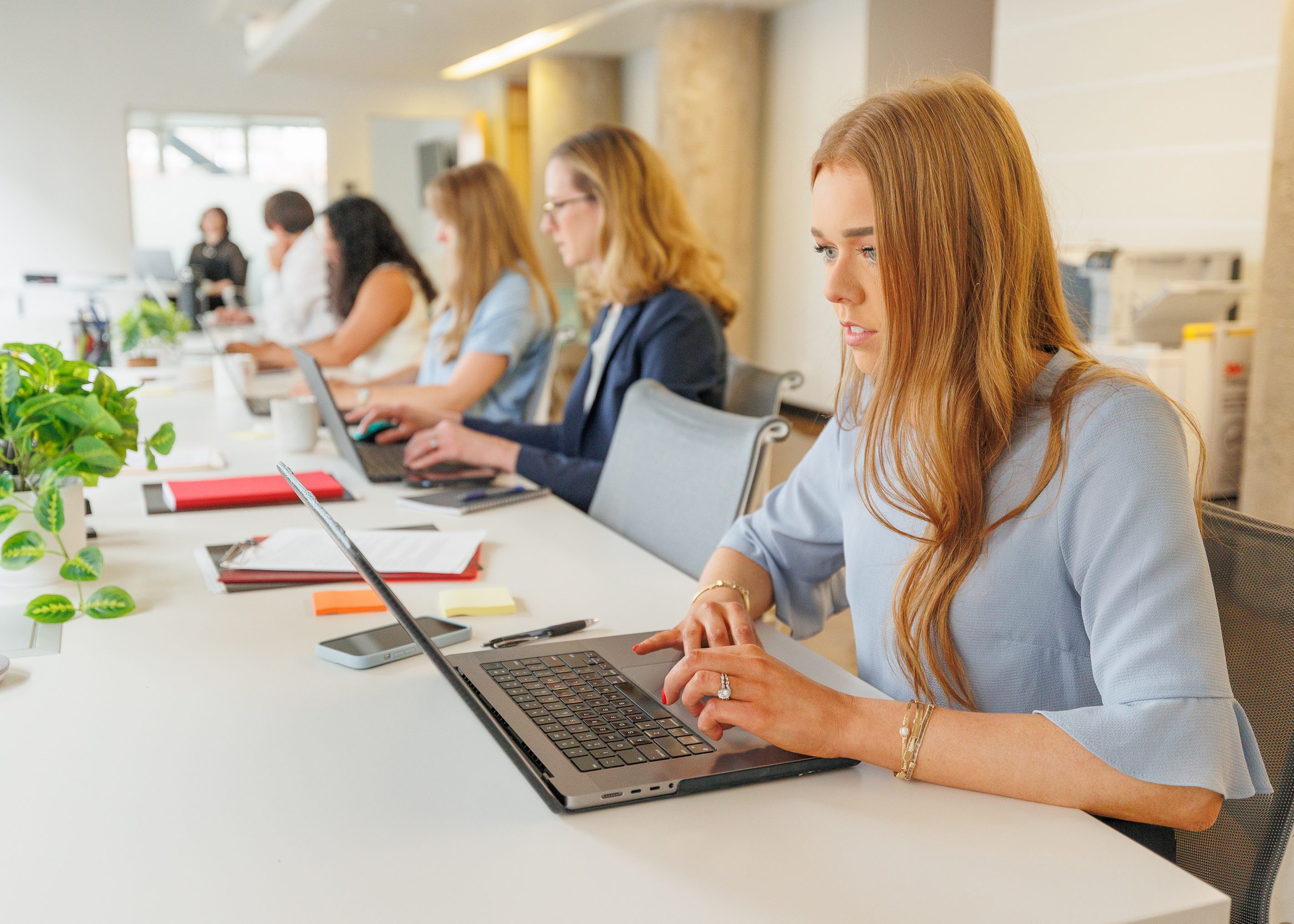 A woman working on a laptop at a table, showing concentration in an office environment.