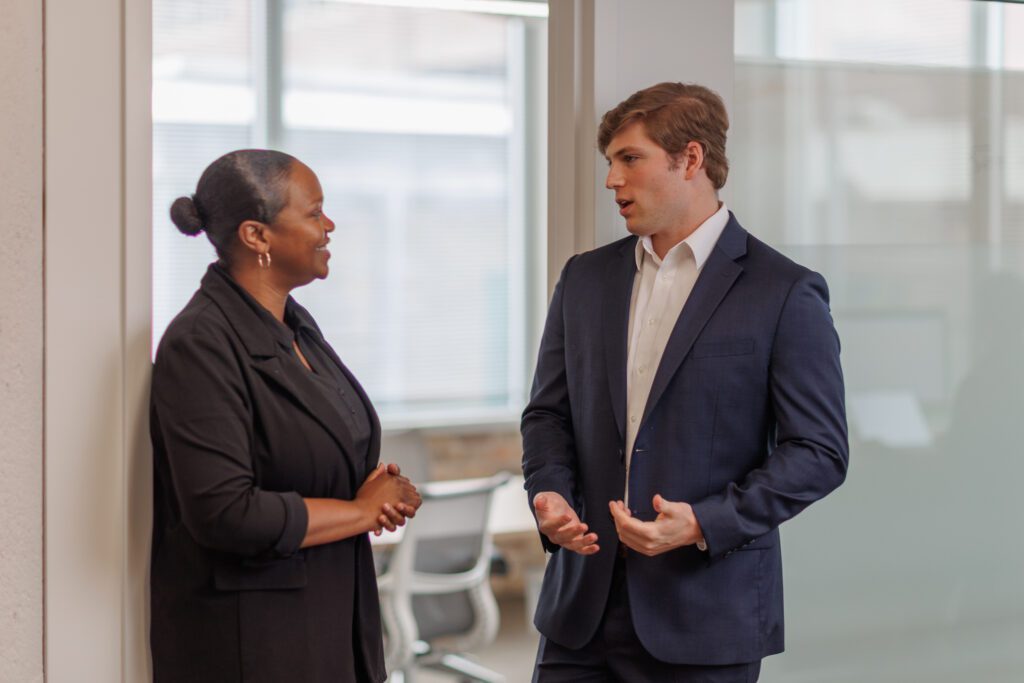 Man and woman wearing business attire standing outside an office conference room talking.